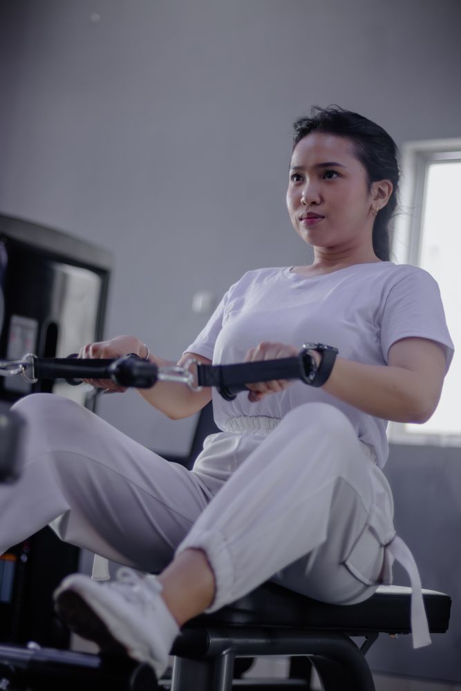 Dedicated young woman strengthening core muscles with rowing mac
