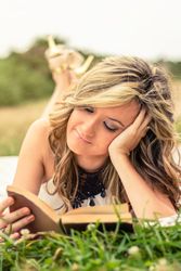 Romantic woman reading a book lying down outdoors