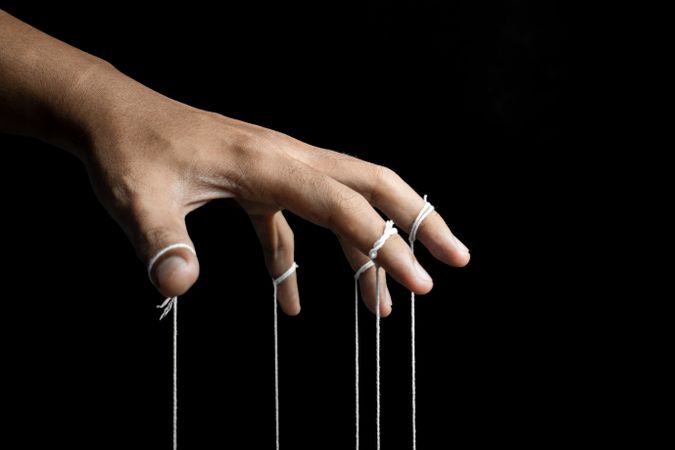 male puppeteer hand with strings isolated on dark background. manipulation or controlling concept