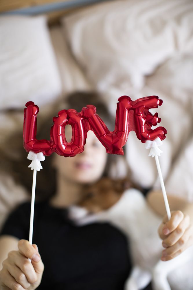 Close up shot of a red balloon that spells “love” with a woman and dog snuggling in the background