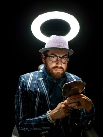 Fashion man in hat holding hand mirror and looking at camera