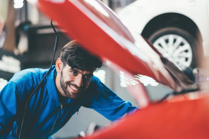Smiling male mechanic working on engine in vehicle