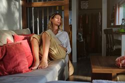 Pensive barefoot woman sitting on couch with notepad
