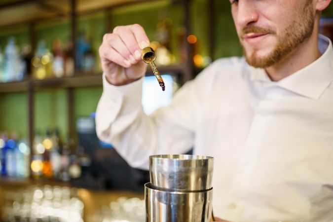 Bartender adding bitters into a shaker for cocktail
