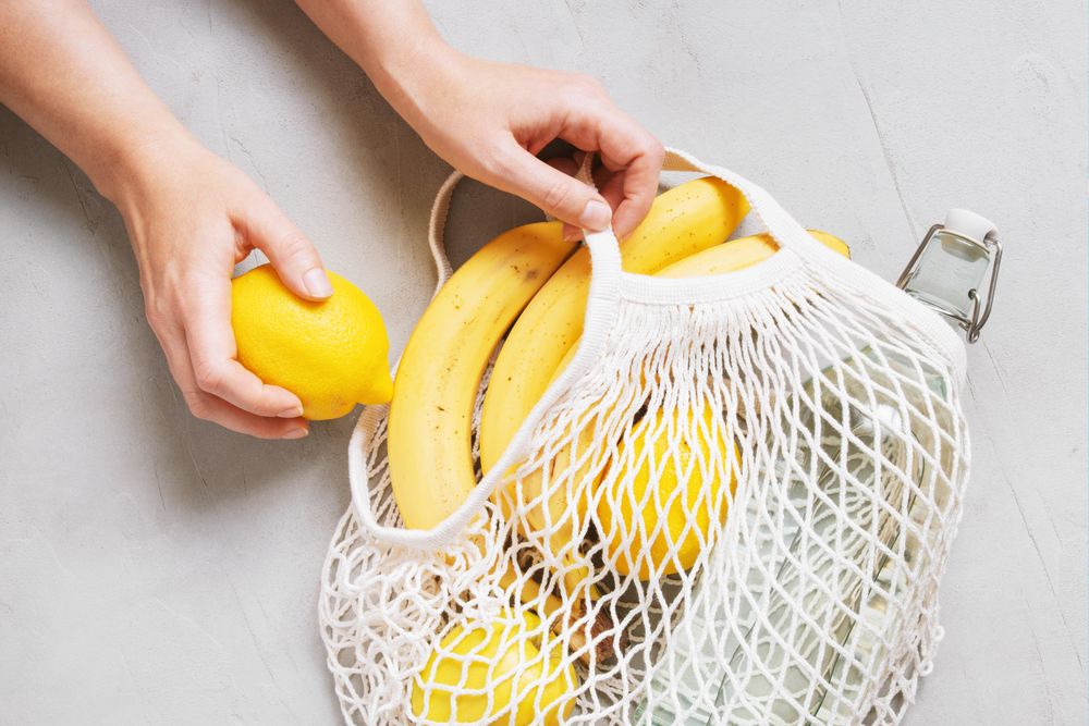 Hands reaching for yellow fruits in mesh back on grey table