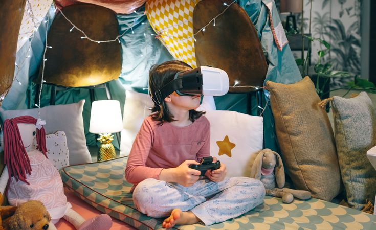 Portrait of girl wearing pajama using VR headset to play in futuristic augmented game at home