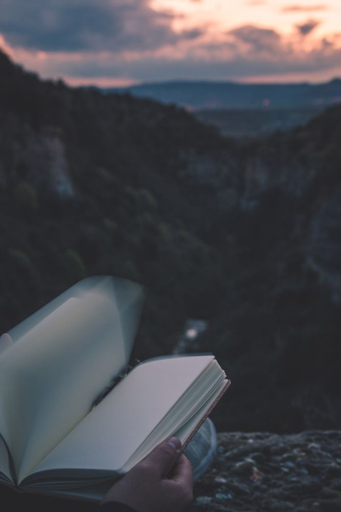 View to small river in canyon and legs of person with book sitting on the edge
