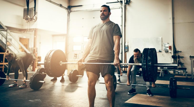 Healthy man deadlifting barbell in busy gym