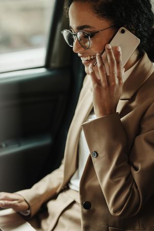 Businesswoman sitting on back seat of car using laptop and phone