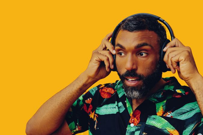 Smiling Black male in bold patterned shirt putting on headphones in yellow room, close up