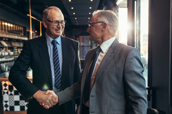 Two mature businessmen meeting at cafe shaking hands
