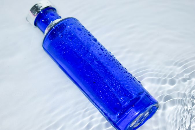 Blue glass bottle on light background with water ripples