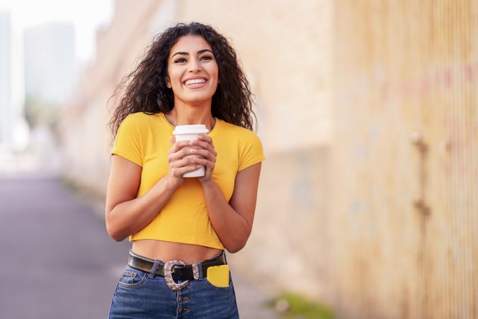 Female in yellow t-shirt walking on street with coffee, copy space