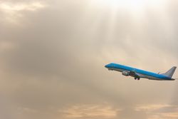 Blue airplane flying through cloudy sky with sun rays