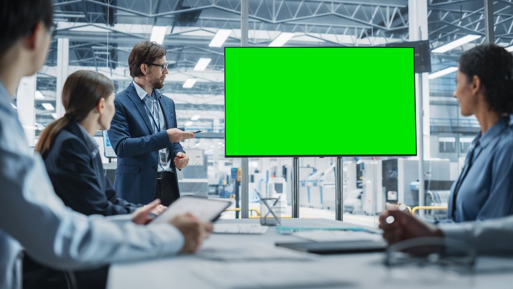 Electronics Factory Office Meeting: Male CEO Presenting Innovative High-Tech Device On TV With Green Screen Chromakey.