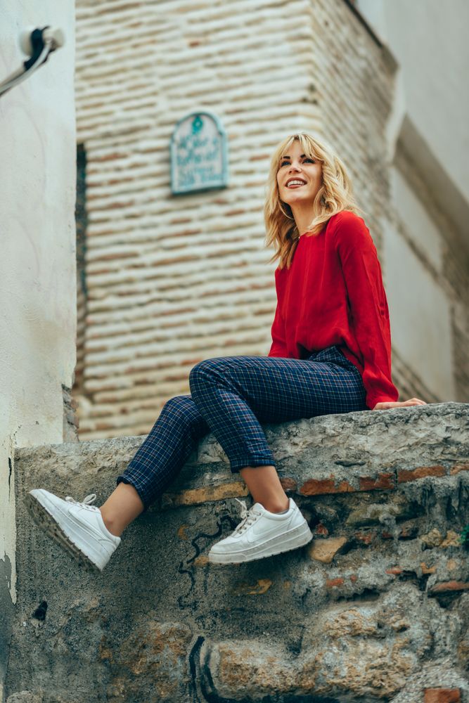 Smiling blond woman in red sweater sitting on stone wall