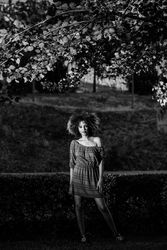 B&W shot of confident woman in dress standing in park looking at camera, vertical