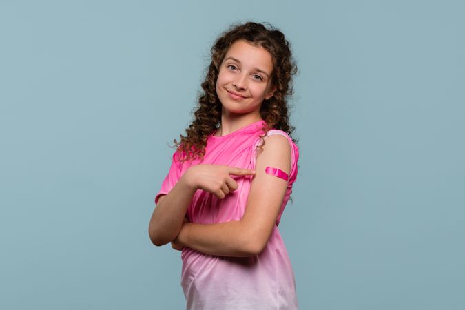 Girl pointing at pink bandage on arm after receiving vaccine.