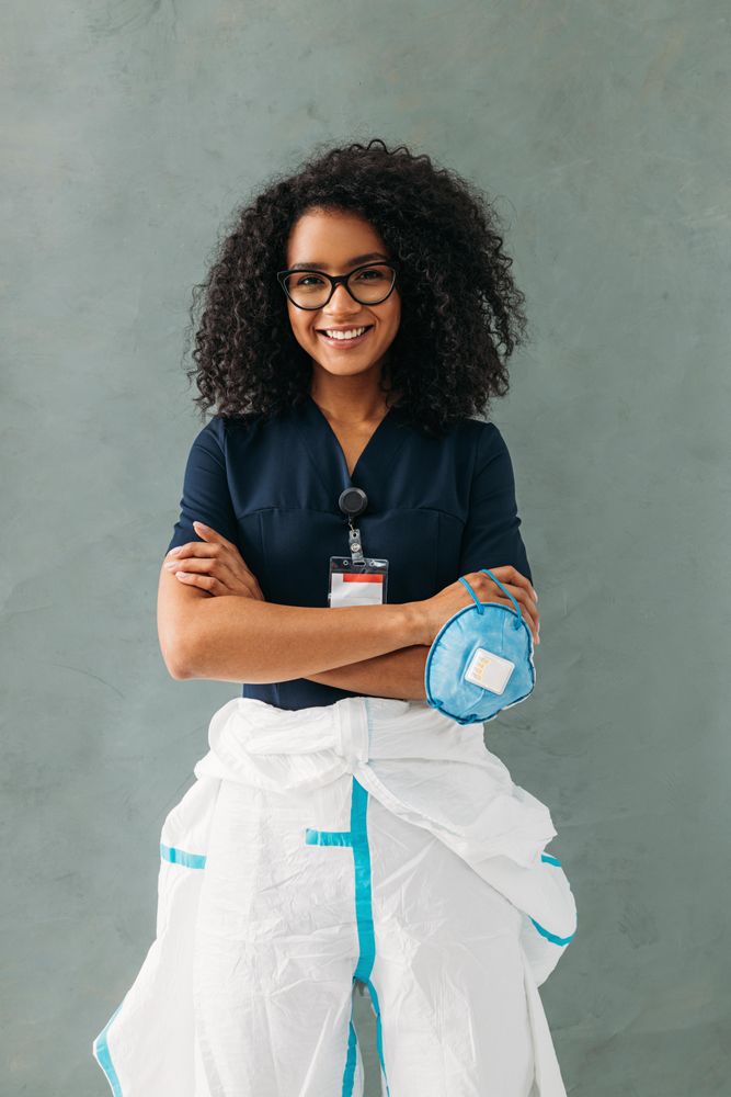 Smiling medical professional holding facemask with hazmat suit on the bottom half of her body