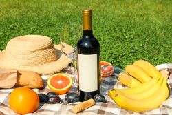 Bottle of wine, baguette, fruits, straw hat and towel on grass, space for text