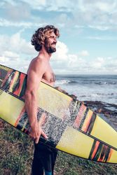 Happy male surfer with board smiling on coast near waves