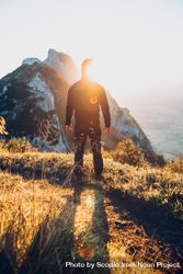 Back view silhouette of a man standing on brown grass facing the sun and mountains bEXgn4