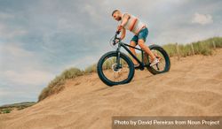 Male riding bicycle down sandy dune 5p2lwb