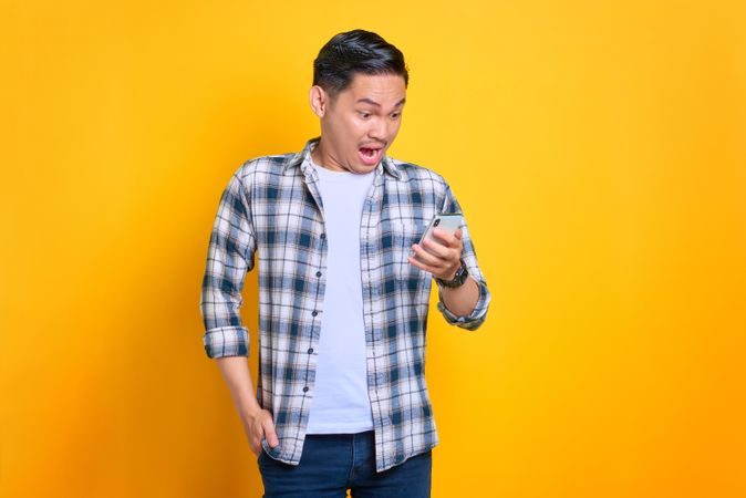 Amazed Asian male looking down at his phone in studio shoot with copy space