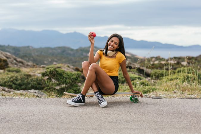 Hispanic cheerful woman with crossed legs sitting on longboards