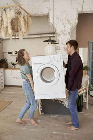 Enthusiastic couple carrying washing machine into new kitchen
