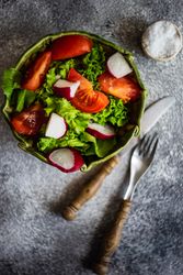 Top view of salad with tomatoes, radish & lettuce on concrete background with copy space