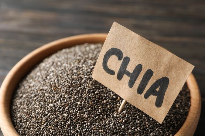Wooden bowl and word Chia on wood background, close up