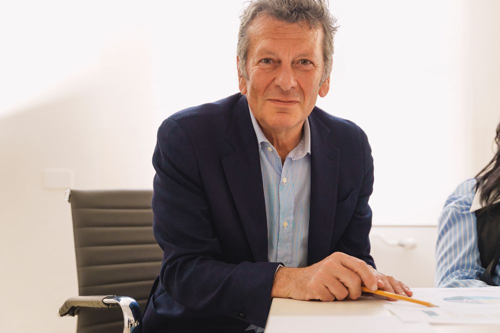 Portrait of a mature businessman sitting at his desk, pencil in hand, looking at camera, with pie chart reports in front of him
