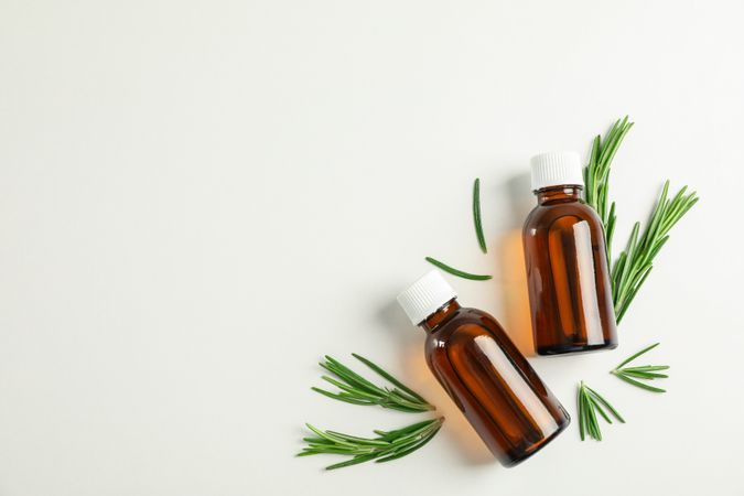 Flat lay composition with rosemary oil and leaves on plain background, space for text