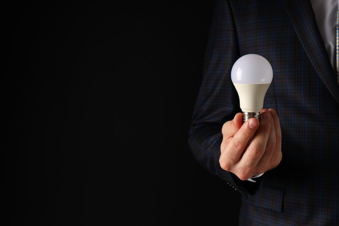 A businessman's hand holds a light bulb on a dark background
