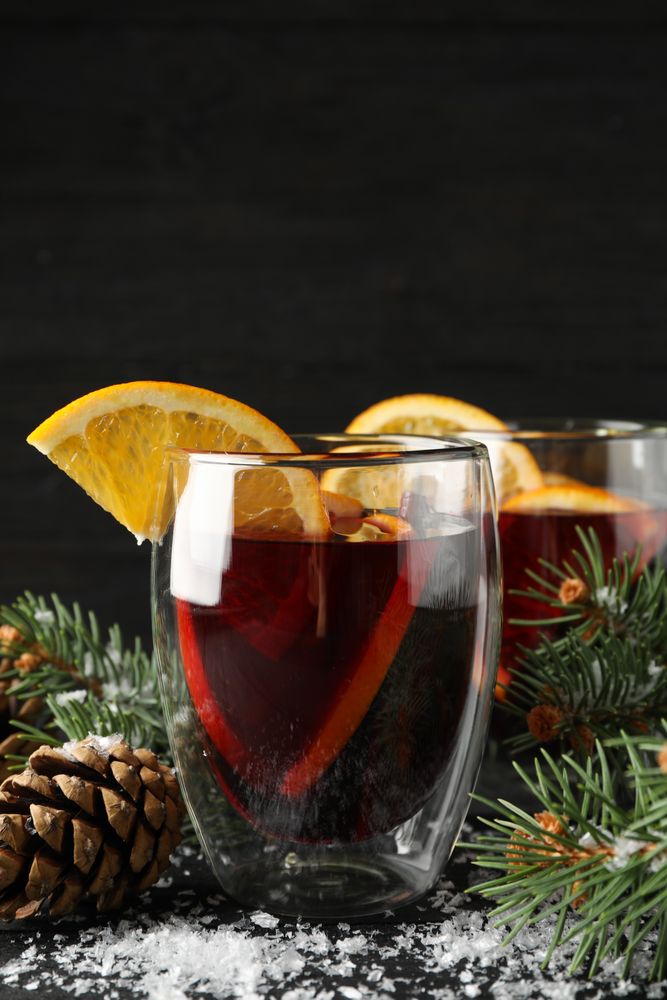 Glasses of tasty mulled with orange on decorated background, space for text