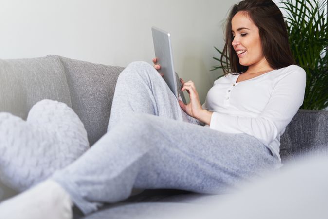 Smiling woman browsing on tablet and sitting on settee