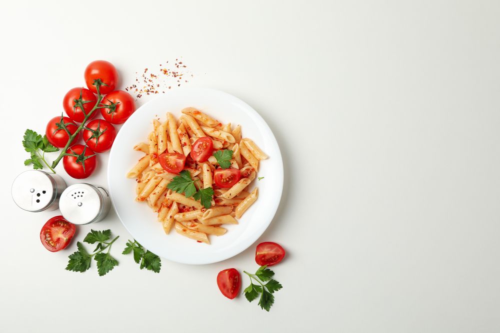 Composition with plate of tasty pasta and ingredients for cooking on blank background