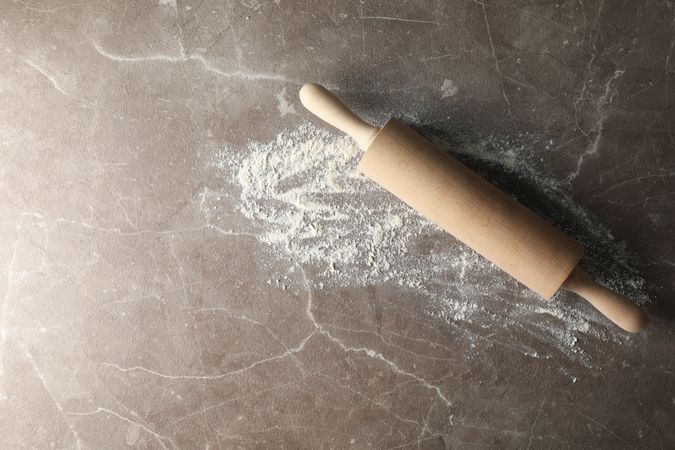 Rolling pin and flour on gray background, top view