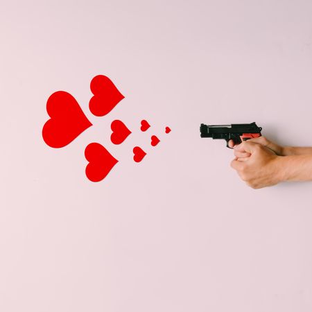 Pistol firing hearts on light pink background