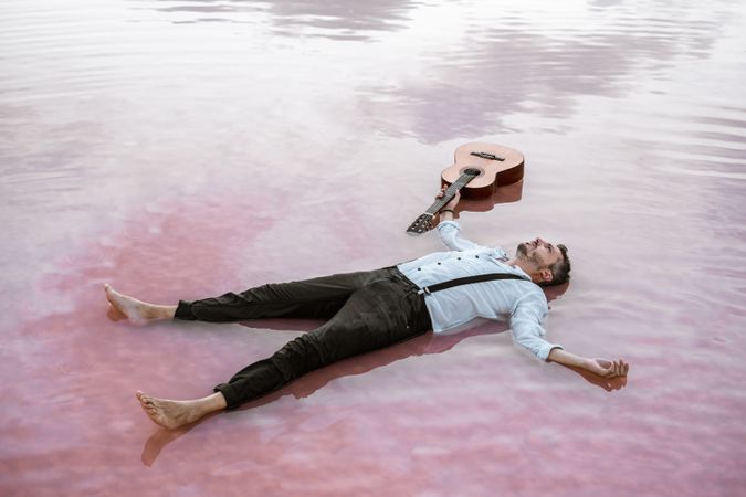 Man resting in water with guitar at seaside
