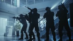 Masked Squad of Armed SWAT Police Officers Stand in Dark Seized Office Building with Desks and Computers.