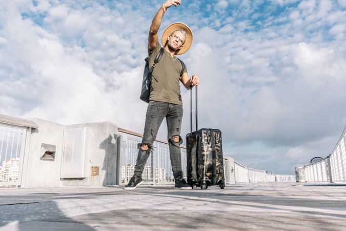 Full length portrait of a hipster man taking a selfie with a suitcase