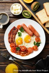Wooden table with breakfast plate of coffee eggs, tomatoes, sausage and bacon, vertical 4jqv95