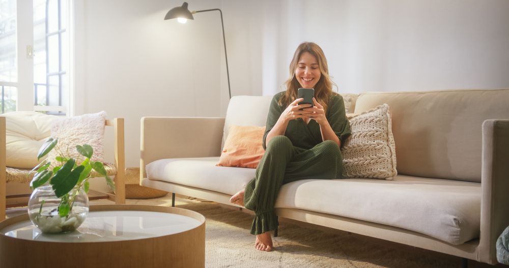 Portrait of Female Using Smartphone in Stylish Living Room while Resting on a Cozy Couch Sofa.
