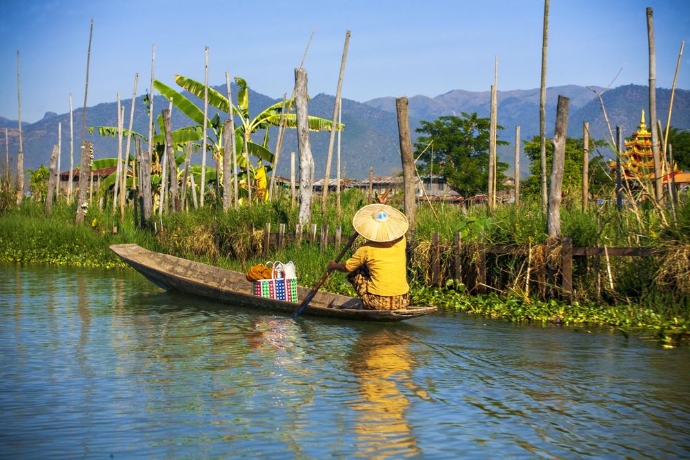 Back view of person in conical hat on a boat in river