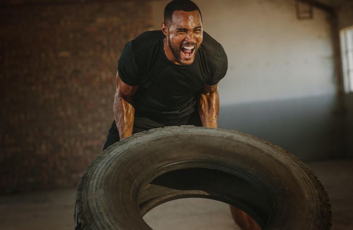 Male athlete flipping heavy tire inside an abandoned warehouse