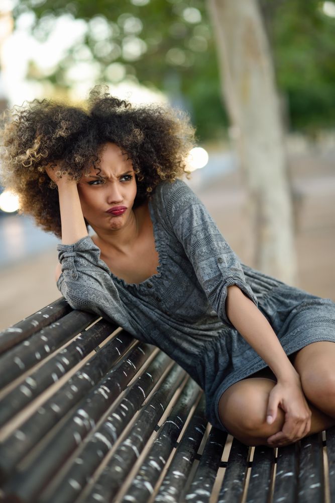 Befuddled female in casual dress sitting on park bench looking around, copy space