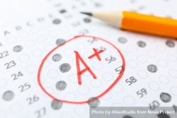 Pencil laying on completed multiple-choice exam with a A+ grade 49ZP6b