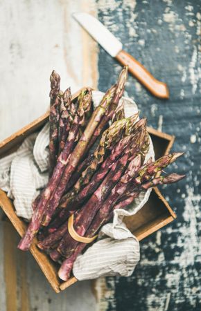 Close up of bunches of purple asparagus, knife on blue background, vertical composition